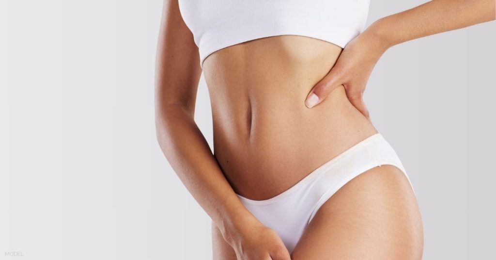 A woman's stomach with their hands on their hips. (Model)